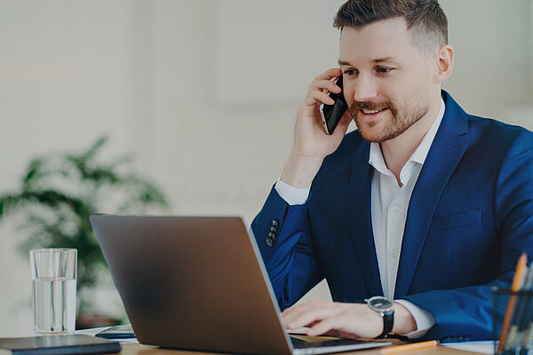 A man on the phone while looking at a laptop