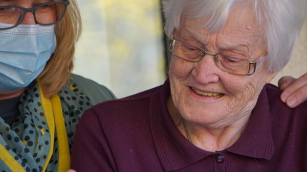 Elderly woman looking at a phone help by a carer.