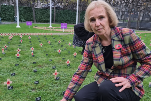 Susan Murray in a green and red tartan suit jacket with a poppy on it in the Garden of Remembrance in Westminster.