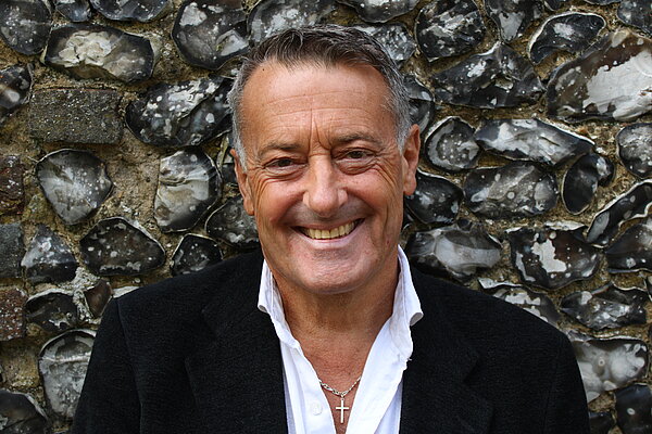 Edgar Hill is standing in front of a wall, smiling and looking directly at the camera.
