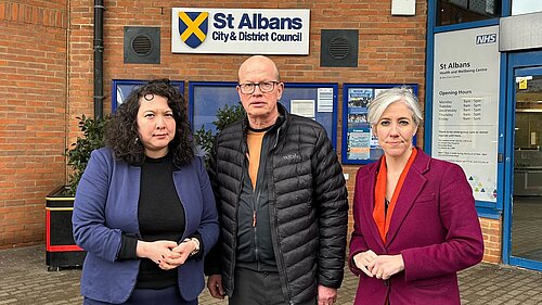 Victoria, Paul and Daisy (from left to right) are standing in front of the St Albans District Council building. They have serious expressions.