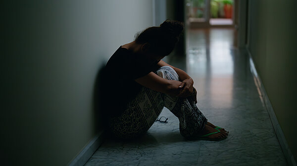 A woman sits on the floor in a dark corridor