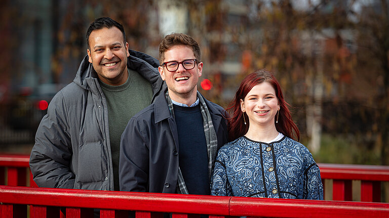 Vikas, JK and Sorcha stood on a red bridge with Canada Water in the background