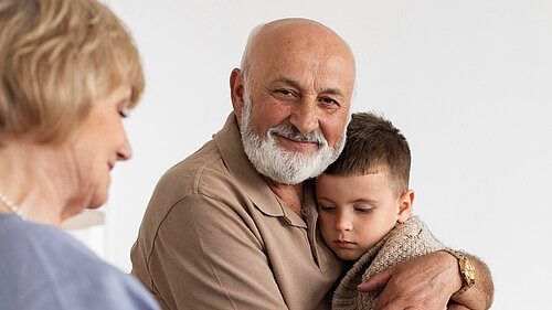 An older man hugs a young child, sat next to him is an older woman