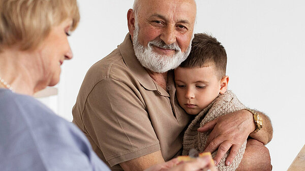 An older man hugs a young child, sat next to him is an older woman