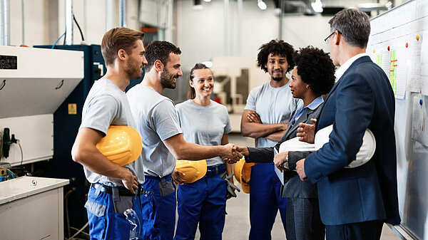 A group of workers in a factory. Two people are shaking hands.