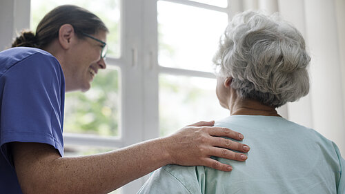 A carer helps an elderly woman to stand