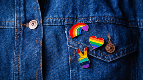 A close crop of a denim jacket with multiple LGBT flag and pride related pins