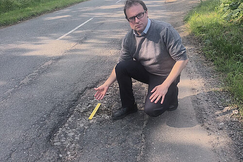 Henry Vann kneeling beside a large pothole