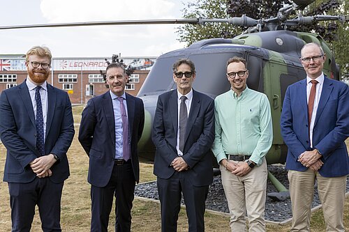 Adam Dance MP stands with four people in front of a military helicopter at Leonardo's Yeovil site