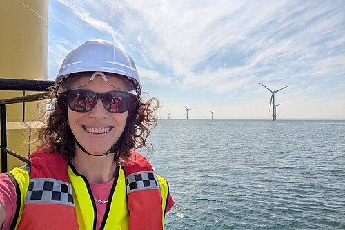 Alison in Hard Hat at Rampion wind farm with the sea stretching out into the background and several turbines