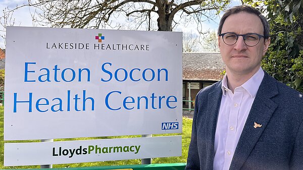 Ian Sollom standing next to the Eaton Socon GP surgery sign