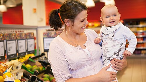 A lady carrying a baby in a supermarket.
