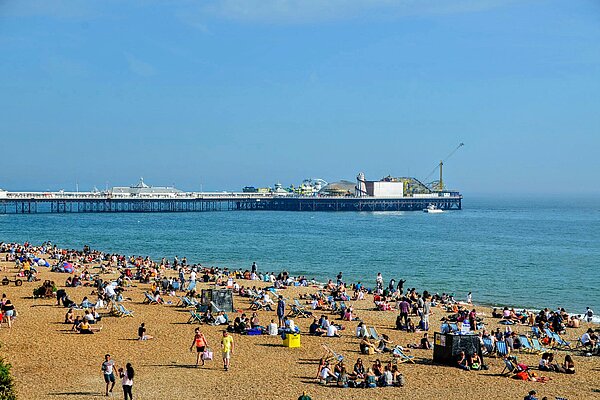 Brighton beach and pier. People are sat on the beach.