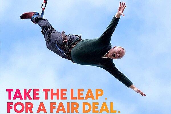 Ed Davey bungee jumping. His arms are spread wide and his mouth is open as he shouts "Vote Liberal Democrat". Text in a magenta-gold gradient reads "Take the leap. For a fair deal."