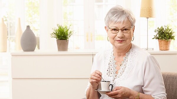 An elderly lady smiling whilst holding a cup of tea.