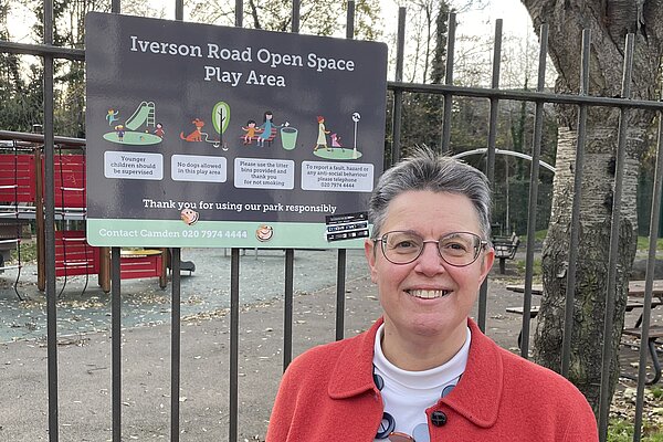 Janet Grauberg. Janet is wearing a red jacket, she is photographed stood in front of a sign reading 'Iverson Road Open Space'