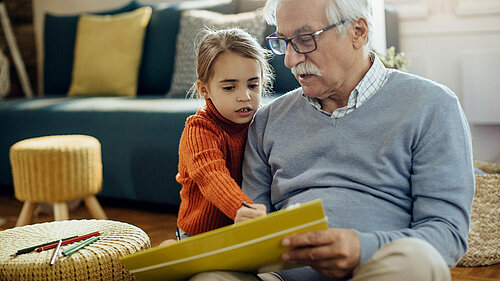 A young child is sat next to an older man, the child is pointing at a book held by the man