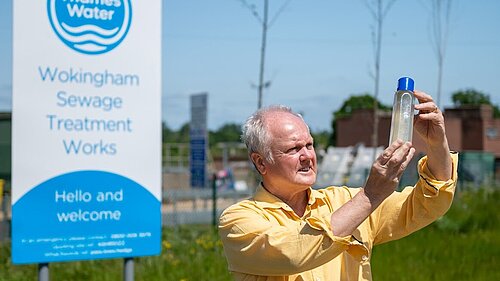 Clive Jones stood outside of Thames Water Wokingham Sewage Treatment Works holding a transparent container filled with contaminated river water.
