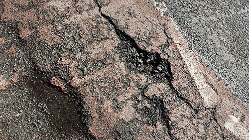 A couple of pot holes in on a damaged road surface