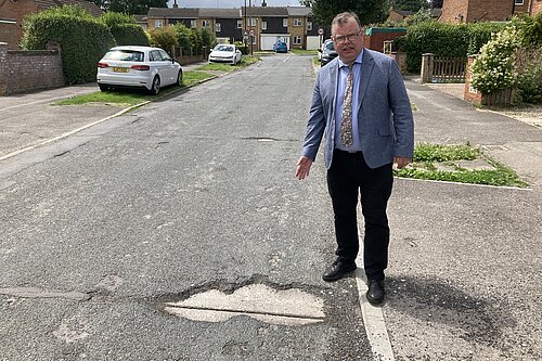 Cllr Waller on Lowfields Drive, pointing at a pothole