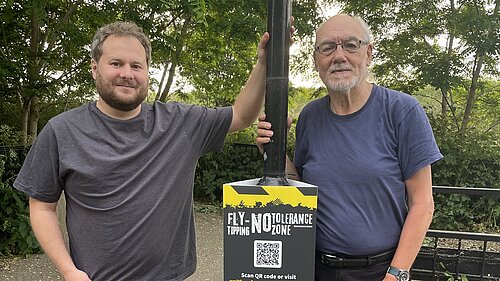 Liberal Democrat campaigners Alex Lewis and Alan Jones standing by a new fly-tipping sign
