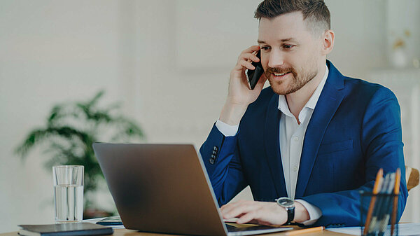 A man on the phone while looking at a laptop