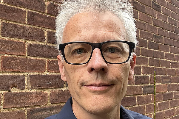 Jesus Pastor is standing in front of a brick wall, smiling and looking directly at the camera.