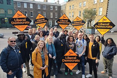 A group of Liberal Democrats froma cross London standing in a group in Bermondsey square with some large orange diamonds