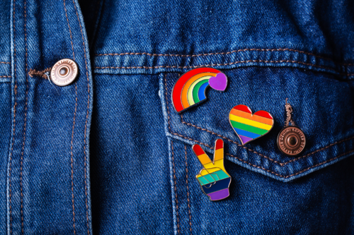 A close crop of a denim jacket with multiple LGBT flag and pride related pins