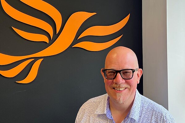 Stephen Gosling. in the background of the photo is a black wall with a Liberal Democrat logo painted on it.