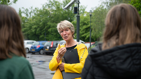 Pippa Heylings talking to two local residents, standing in a car park in the rain