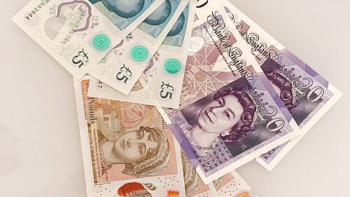 Seven pound coins on top of a ten pound note.