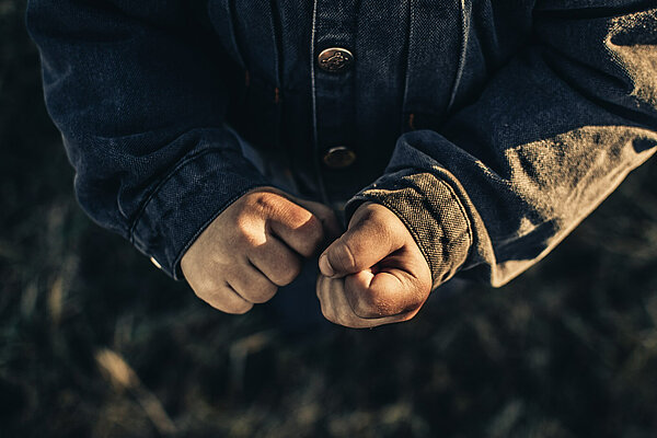 Photo shows a person's clenched fists, they are wearing a grey jacket.