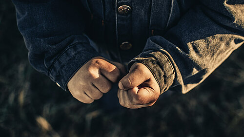 Photo shows a person's clenched fists, they are wearing a grey jacket.