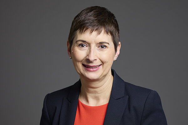 Caroline Pidgeon. Caroline is photographed wearing a black jacket over a red dress, against a plain grey background.