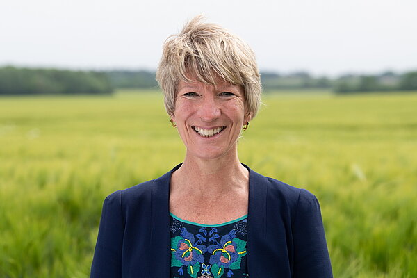 Head and shoulders photo of Pippa Heylings, Lib Dem Parliamentary candidate for South Cambs. Pippa is smiling at the camera, standing in front of a grassy field with trees in the distance.