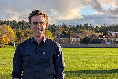 Torso shot of Ben Dempsey in front of a playing field with houses behind it.