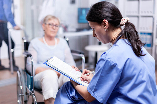 A doctor writes on a clipboard while a patient waits